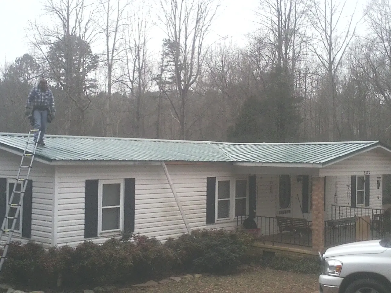 Worker on a ladder beside a new green metal roof on a ranch home in West Haven