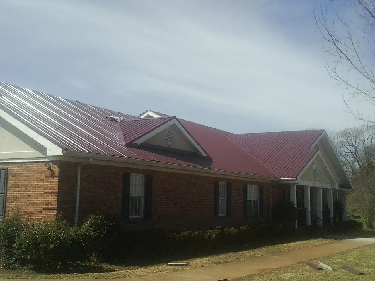 Red metal roof with gabled entries on a long brick building, from a Hail Damage Roof Repair job in West Haven