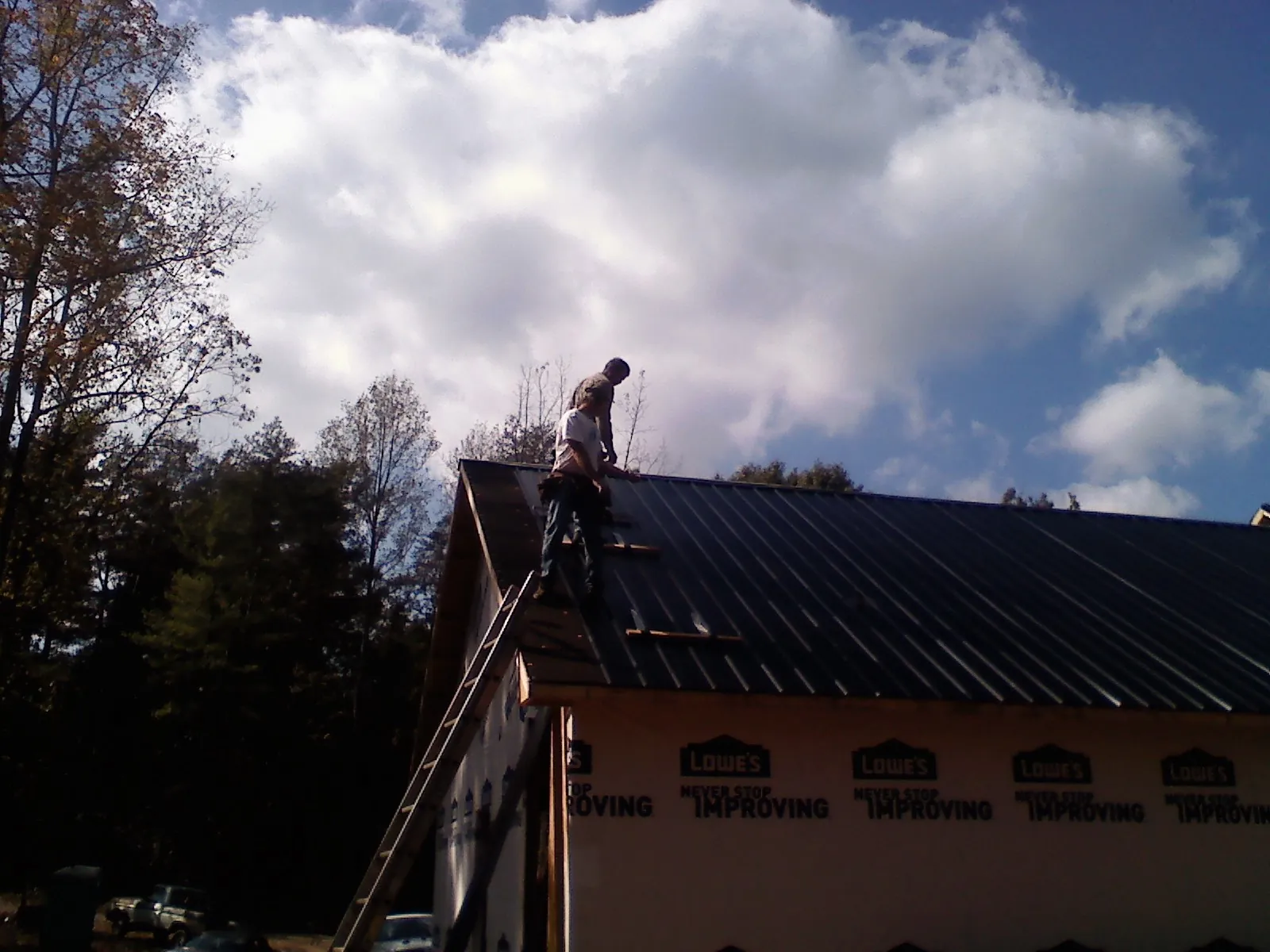 Roofer fastening dark metal panels high against a cloudy sky, from a Roof Inspection job in West Haven