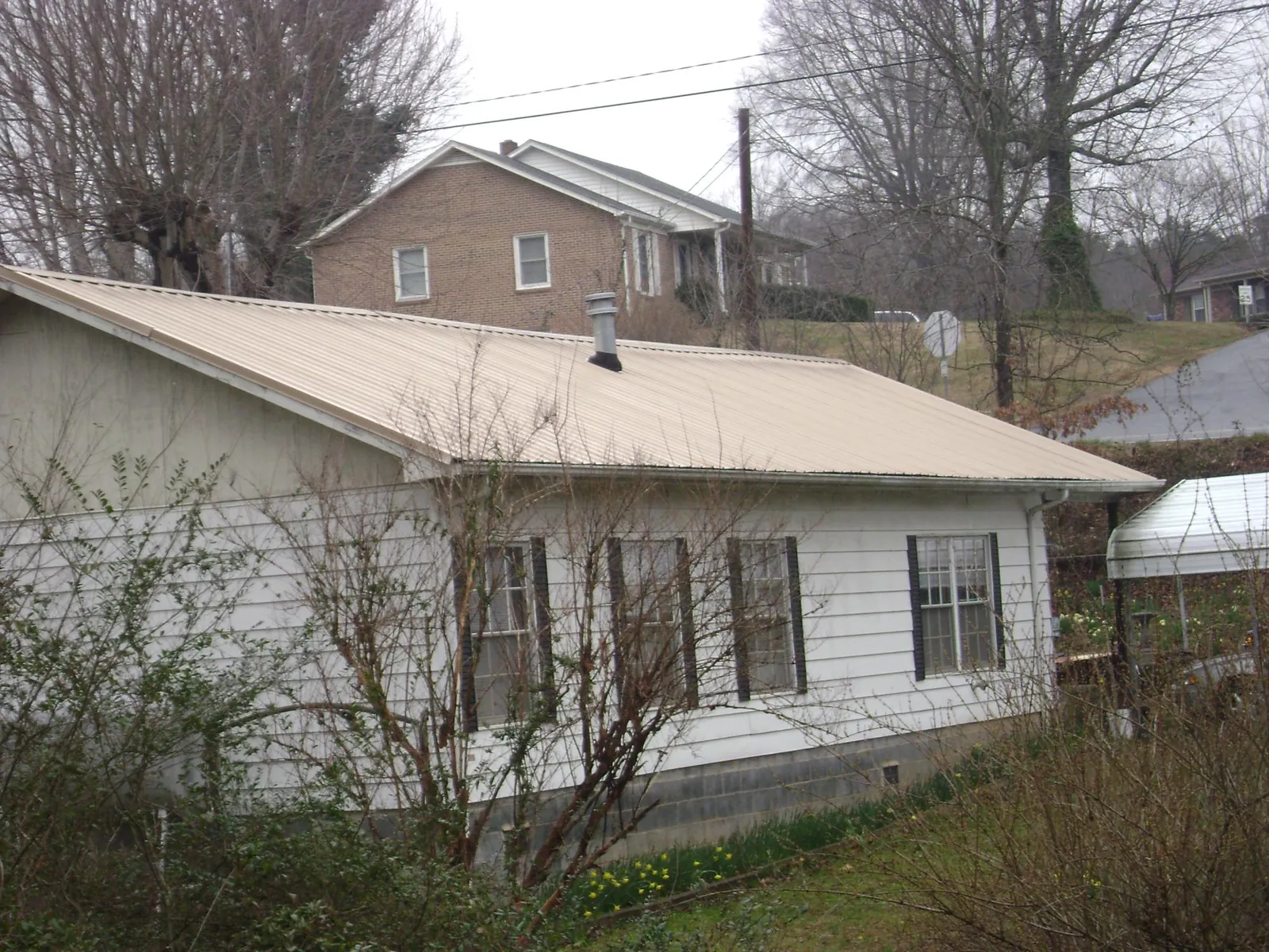 Tan metal roof on a white sided house set into a hillside — Commercial Roofing by Roofing Brothers in West Haven